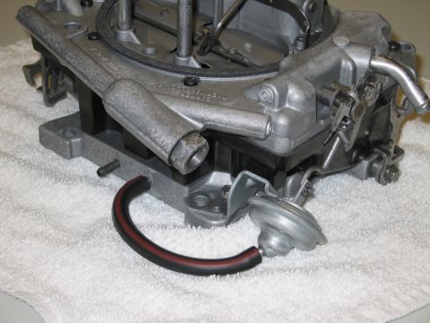 1991 Ford LTD Crown Victoria - underside of a four-barrel carburetor on a white towel, showing throttle bores, a vacuum diaphragm and a curved hose.
