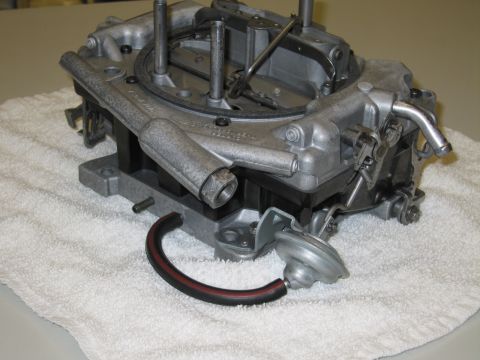 1991 Ford LTD Crown Victoria - carburetor viewed from below on a white towel, with throttle bores, a vacuum diaphragm and a black-and-red hose.