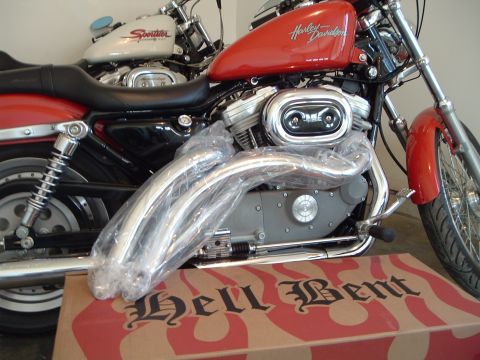 2002 Harley-Davidson Sportster Custom - A red 2002 Harley-Davidson Sportster Custom motorcycle is shown in a 3q-front view, with new chrome exhaust pipes in plastic wrap.