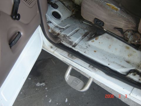 1993 Ford Bronco - The interior of a white vehicle shows a worn door panel, rusty floor, and a torn seat.