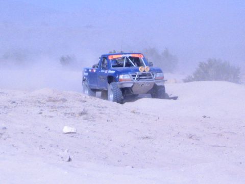 Blue off-road race truck with KC lights climbing a sandy berm in the desert