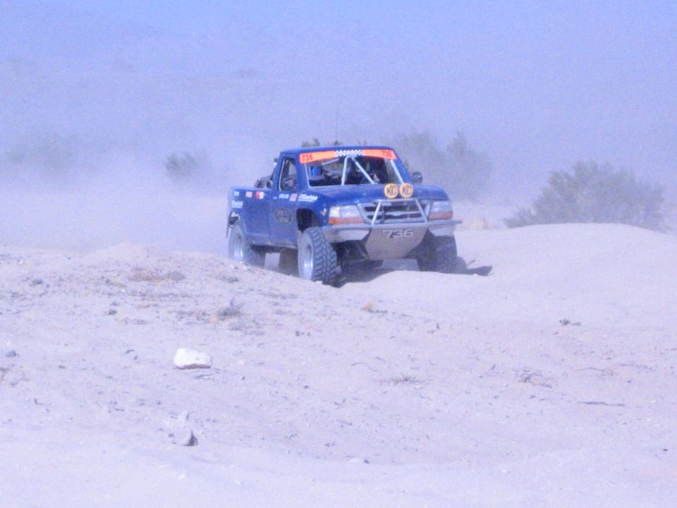 Blue off-road race truck with KC lights climbing a sandy berm in the desert