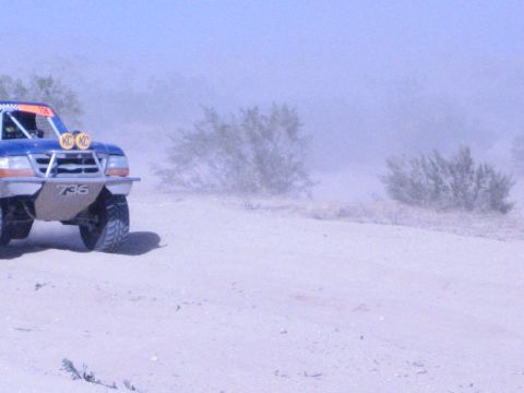Front corner of blue off-road race truck 736 with yellow lights in desert dust