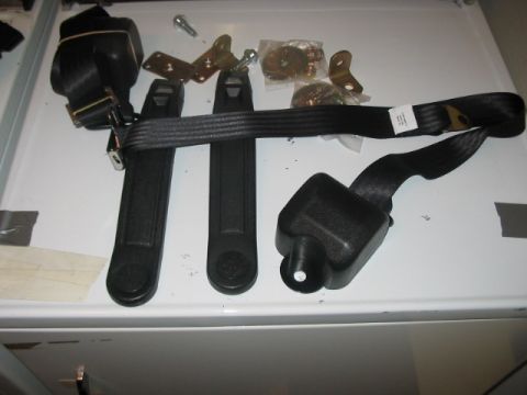 1991 Ford Bronco - Seat belt parts laid out on a white surface, including retractors and hardware.