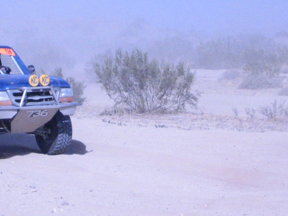Front of blue race truck 736 with yellow KC lights beside desert brush