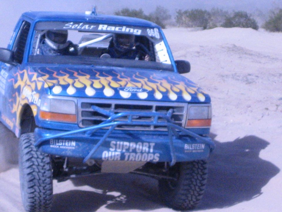 Blue flame-painted Ford race truck with Support Our Troops bumper in desert
