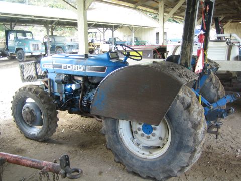 1968 Ford Mustang - A blue Ford tractor is parked under a covered structure with other vehicles in the background.