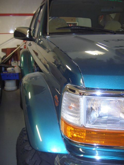 1996 Ford Bronco - Close-up of a teal Ford Bronco's front quarter panel, revealing its distinctive body style and headlight configuration.