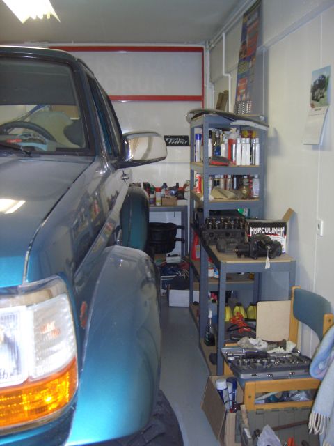 1996 Ford Bronco - A teal 1996 Ford Bronco is parked in a garage, with shelves of supplies and tools visible in the background.