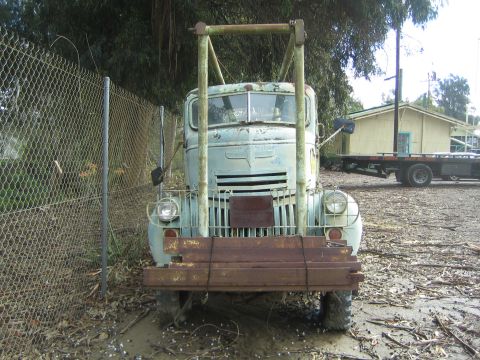 1968 Ford Mustang - An old truck sits in a muddy lot, partially obscured by a chain-link fence and foliage.