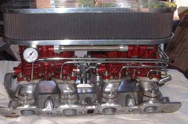 Dual carb intake manifold with chrome air cleaner and a pressure gauge. The manifold is red and polished aluminum