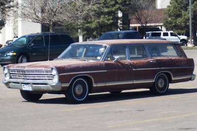 1972 Ford Ranchero - Station wagon with significant rust damage is parked in a lot.