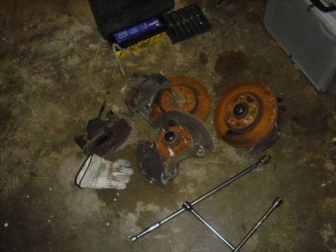 1986 Ford Mustang - Disassembled car brake components and a lug wrench lie on a dirty concrete floor next to a toolbox.