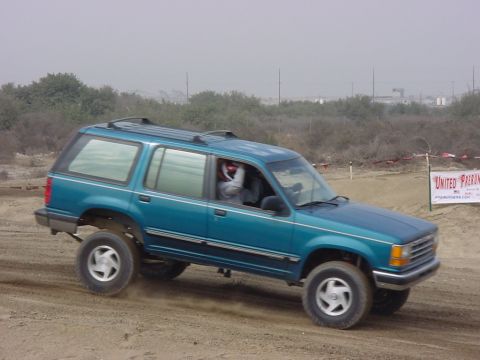 1984 Ford Bronco - A teal SUV with a roof rack is seen from the front-right angle on a dirt track.