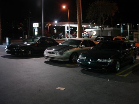 1993 Ford Taurus - Three sedans parked at a gas station at night. The silver car appears to be a Ford Taurus.