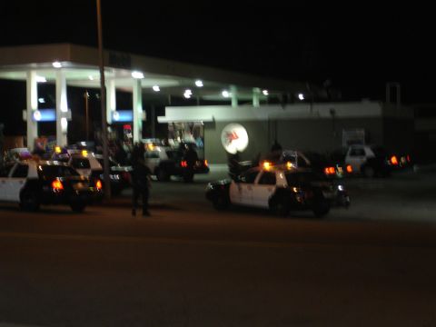 1993 Ford Taurus - Police vehicles are gathered at a gas station under the bright lights of the canopy.