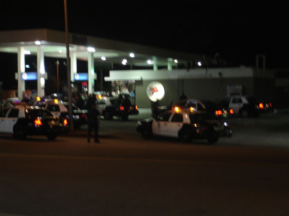 Several police cars are parked at a gas station at night. One car has its lights on