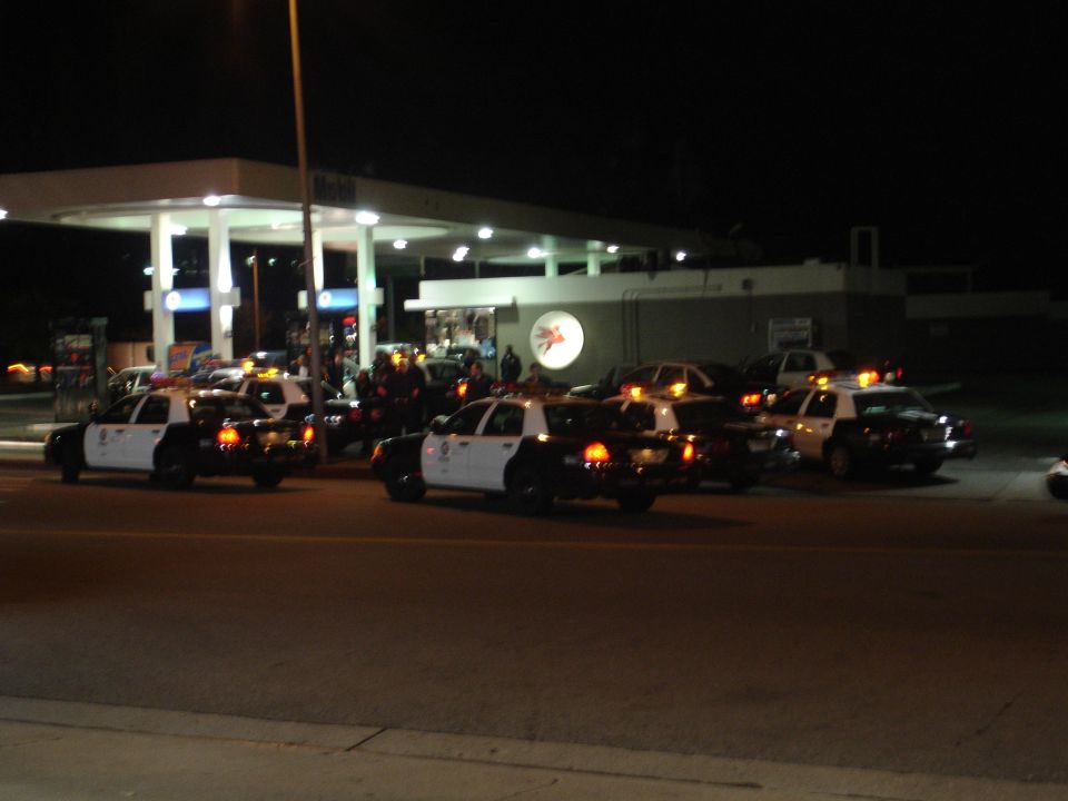 Several police cars are parked at a gas station at night