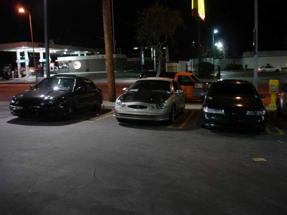 Three sedans parked at night, one with a silver body and black hood