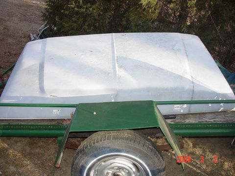 1978 Ford Bronco - A white vehicle hardtop is shown resting on a trailer, with a spare tire visible beneath a green metal support.