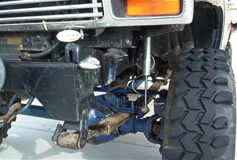 1986 Ford Bronco - Close-up of truck's front suspension and tire, showing leaf springs and shock absorber.