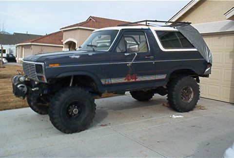 1986 Ford Bronco - Lifted Ford Bronco with off-road tires sits in front of a garage.