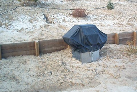 1986 Ford Bronco - An outdoor air conditioning unit is covered by a black tarp in a sandy yard with some snow on the ground.