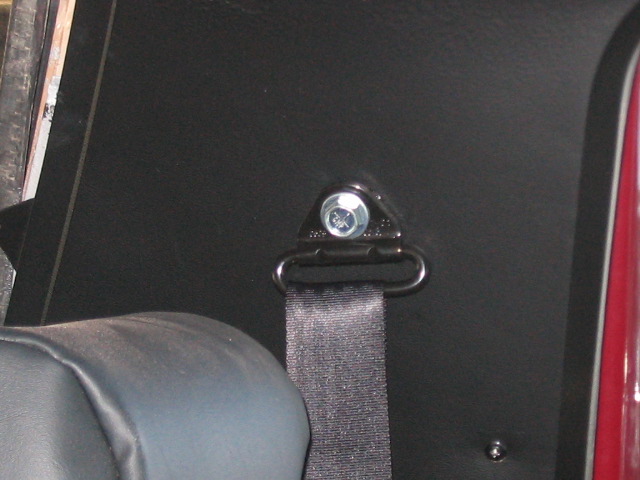 Black seatbelt attached to a triangular metal anchor bolted to a black interior panel