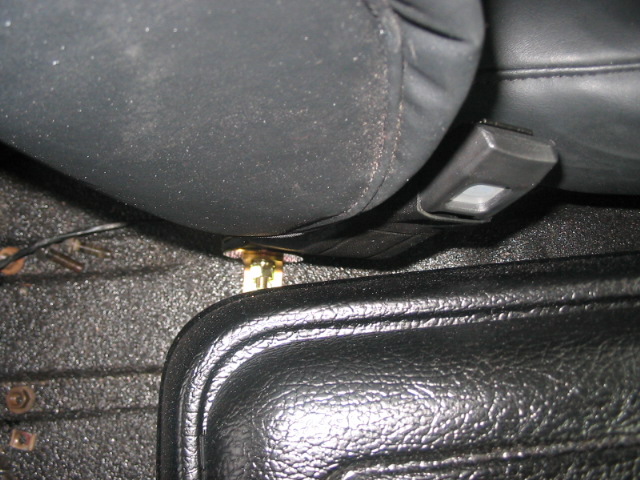 Close-up of a seatbelt buckle and its mounting bolt on a textured floor
