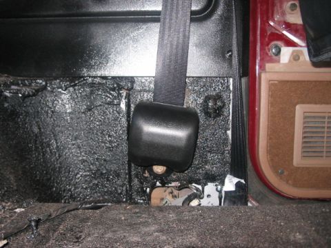 1991 Ford Bronco - Close-up of a vehicle's interior showing a seatbelt mechanism and textured floor.