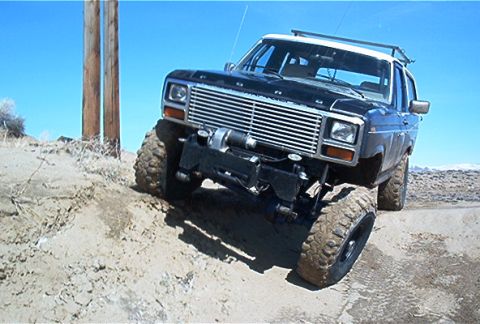 1986 Ford Bronco - A modified Ford Bronco navigates a sandy incline under a clear blue sky.