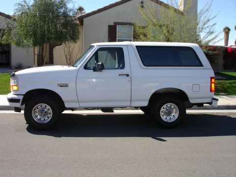 1996 Ford Bronco - A white Ford Bronco SUV is seen from the side, parked on a street in front of a house.