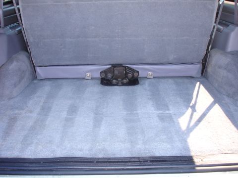 1996 Ford Bronco - The rear cargo area of an SUV shows gray carpeting and a folded seat, with a visible latch mechanism.