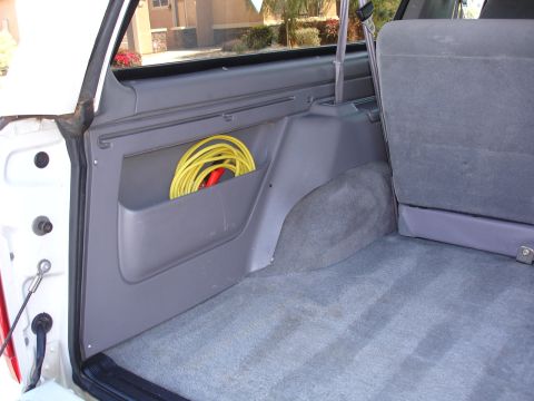 1996 Ford Bronco - The interior cargo area of a vehicle shows a side storage pocket containing a coiled yellow cord.