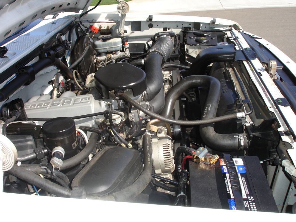 Engine bay of a white Ford truck with 5.0 EFI V8, air intake tube and battery