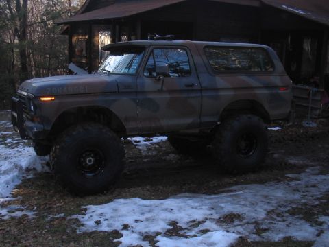 1979 Ford Bronco - This lifted 1979 Ford Bronco features a camouflage paint scheme and aggressive off-road tires, parked in a snowy, wooded area.