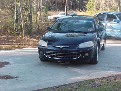 1994 Ford Crown Victoria - A dark sedan is parked on a concrete surface with trees and another vehicle visible.