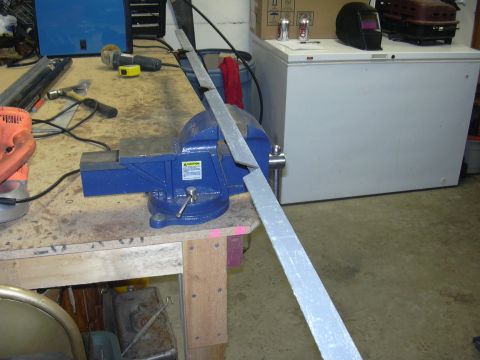 1991 Ford Bronco - A metal bar is secured in a blue vise on a workbench, with tools and a freezer in the background.