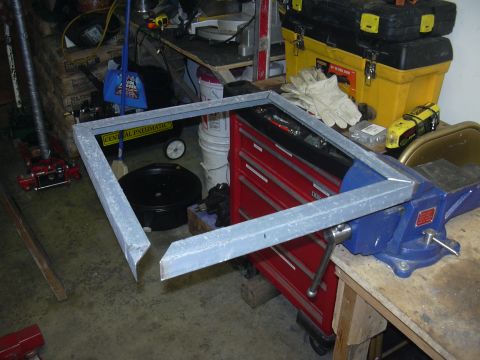 1991 Ford Bronco - A metal frame is secured in a vise, with various tools and equipment visible in the cluttered workshop setting.