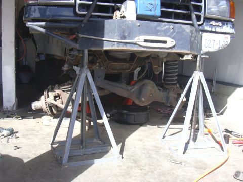 1991 Ford Bronco - Front axle and suspension of a 1991 Ford Bronco undergoing maintenance, supported by jack stands.