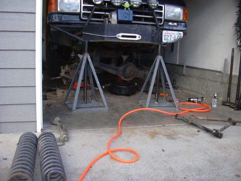 1991 Ford Bronco - A black Ford Bronco is undergoing repairs in a garage, with its front end lifted and parts laid out on the floor.