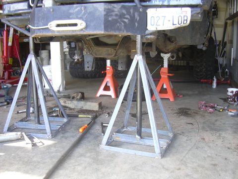 1991 Ford Bronco - A vehicle's rear bumper and undercarriage are elevated on jack stands in a garage, revealing a license plate.
