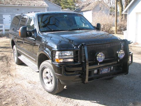 2003 Ford Excursion - This black Ford Excursion is parked on a dirt road in front of a couple of buildings.