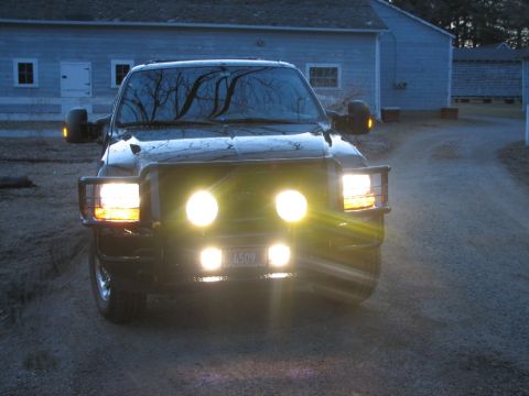 2003 Ford Excursion - A black Ford Super Duty truck is parked in front of a building at dusk, its lights illuminated.