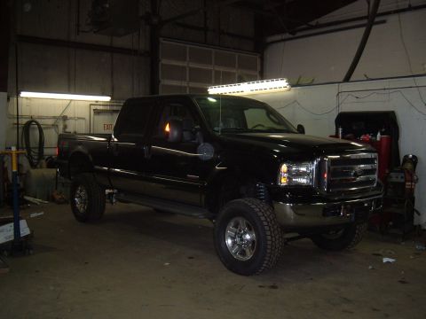 1979 Ford Bronco - A black pickup truck is parked inside a garage, a prominent chrome grille and an overhead light bar.