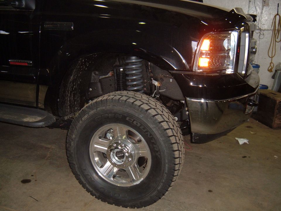 Front corner of black pickup truck, showing tire, suspension, and headlight