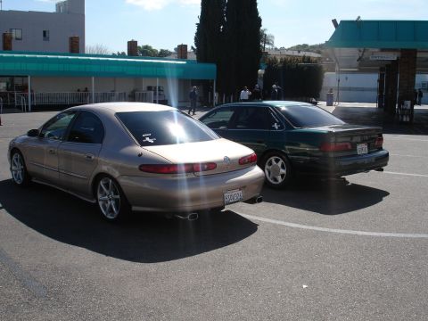 1993 Ford Taurus - Two sedans are parked in a lot, one gold and one green, viewed from the rear.