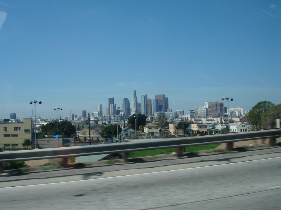 City skyline with skyscrapers under a clear blue sky, seen from a highway overpass