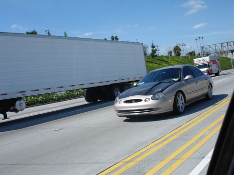 1993 Ford Taurus - A gold sedan with a dark hood drives on a highway next to a large semi-trailer truck.