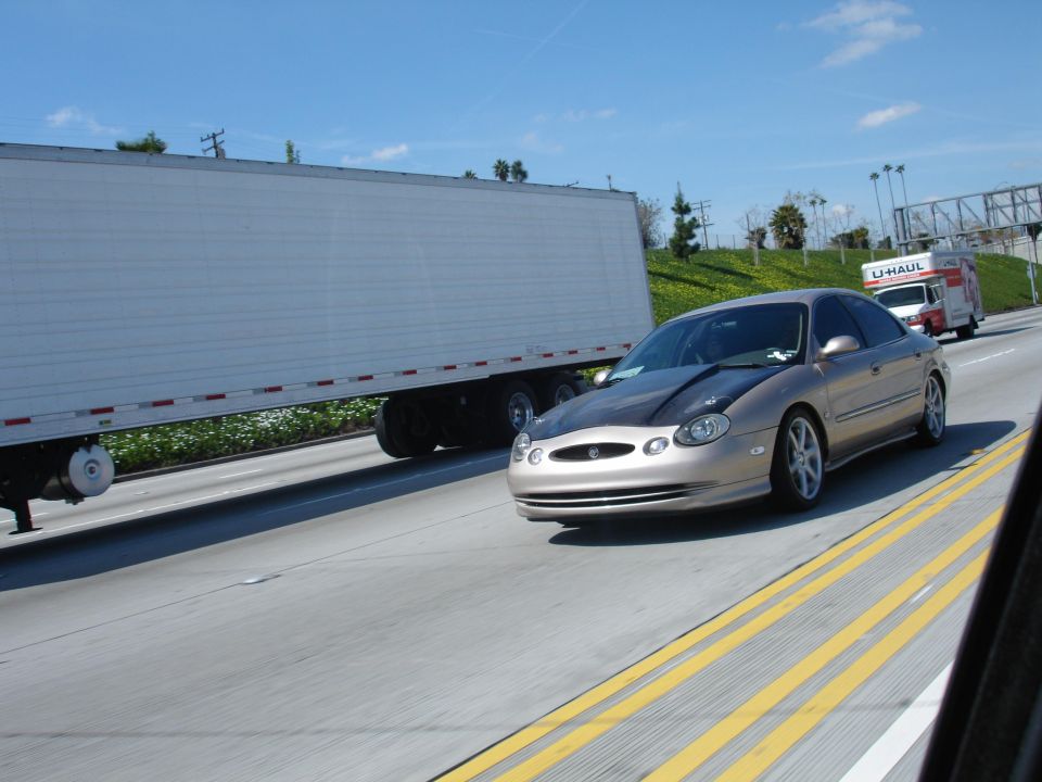gold sedan with dark hood driving on highway next to a semi-trailer truck